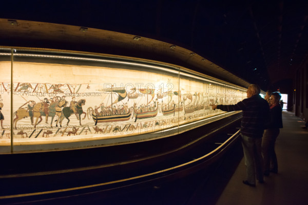 A couple of tourists admiring the Bayeux tapestry or La Tapisserie de la Reine Mathilde in it's current display case