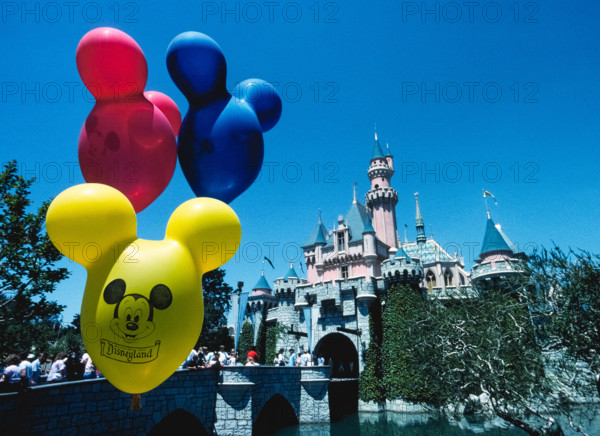 Brightly-colored balloons with the face of Mickey Mouse float in front of Sleeping Beauty Castle, an imposing fairy-tale structure that is the centerpiece of the world’s most famous theme park, Disneyland, which opened in 1955 in Anaheim, California, USA. The building was modeled after a real castle, Neuschwanstein, constructed in Germany in the late 1800s as a palace for King Ludwig II of Bavaria. Disneyland was the creation of Walt Disney, a well-known American entrepreneur and filmmaker who created Mickey Mouse and other iconic cartoon characters.