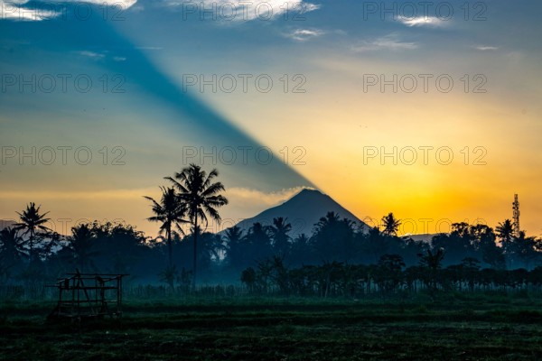 The casts a shadow as it rises over Mt Merapi, an active volcano in Central Java, Indonesia. Smoke spilling from the caldera.