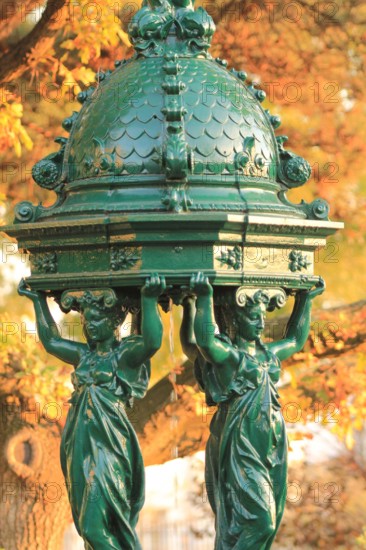 Wallace fountain in Paris by fall / One of the drinking fountains in Paris so called "Wallace fountains" in autumn with yellow foliage as a background