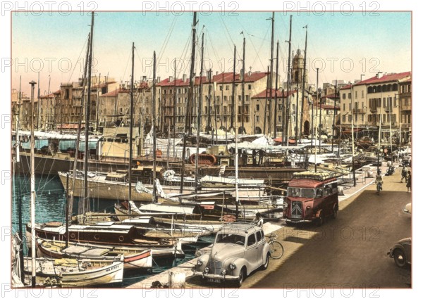 ST.TROPEZ Vintage 1950’s 1960's View of the harbour with fishing and sailing boats moored with French Citroen Van and Peugeot Motorcar parked, cafes and restaurants behind. Côte d’Azur South of France Riviera. Saint-Tropez picturesque, cafe & shop-lined harbour port and a popular trendy chic fashionable sailing & luxury yacht destination.