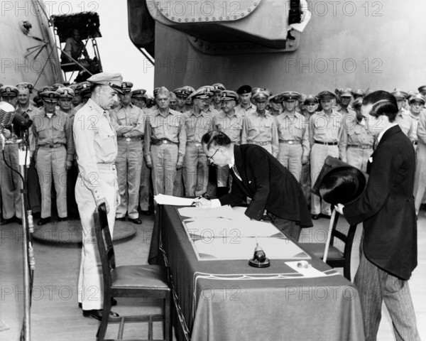 Japanese Foreign Minister Mamoru Shigemitsu signs the Instrument of Surrender on behalf of the Japanese Government, on board USS Missouri (BB-63), 2 September 1945. Lieutentant General Richard K. Sutherland, U.S. Army, watches from the opposite side of the table. Foreign Ministry representative Toshikazu Kase is assisting Mr. Shigemitsu.