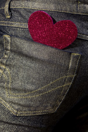 A vibrant red glitter heart-shaped sticker adorns the back pocket of a denim jean, symbolizing casual love and fashion