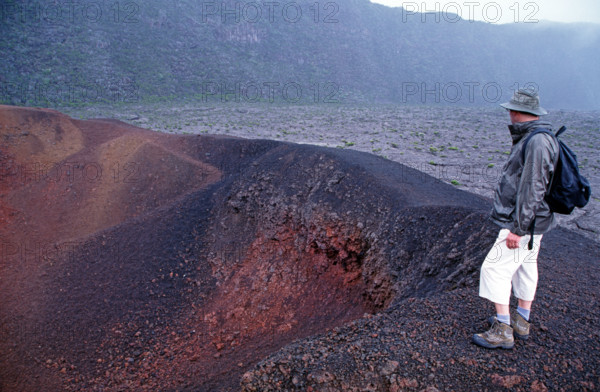 Tourist standing on the edge of Formica Leo crater, Piton de la Fournaise volcano, La Reunion Island, Indian Ocean