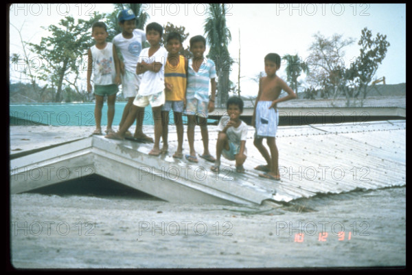 This photograph captures children on a roof in Bamban, Philippines, on December 10, 1991, during the aftermath of the catastrophic eruption of Mount Pinatubo. The eruption caused widespread destruction, with ash clouds affecting nearby areas.
