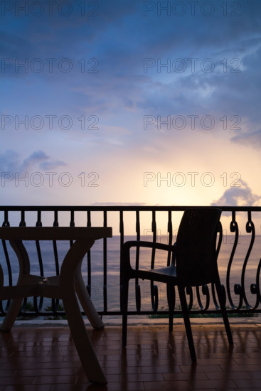 Armchair and table stand on a balcony. Seaside view over bright sunrise sky