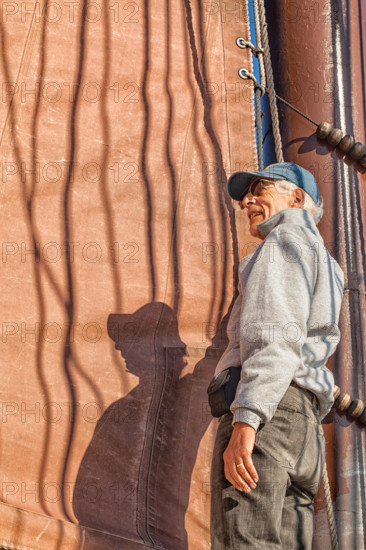 Senior man on a sailboat helps to hoist the sail. Adventure travel on a tall ship schooner. Concept for staying healthy in active retirement.