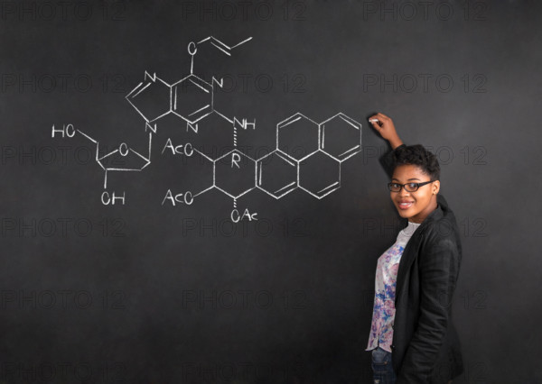 South African or African American woman teacher writing science on chalk black board background
