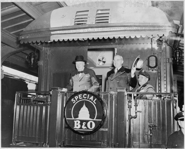 Photograph of President Truman and Prime Minister Churchill standing on the rear platform of a special Baltimore & Ohio train (evidently en route to Fulton, Missouri for Churchill's Iron Curtain Speech), with the President's Military Aide, General Harry Vaughan, seated nearby.
