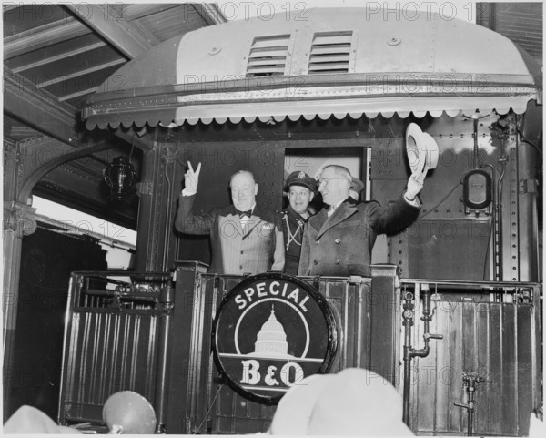 Photograph of President Truman waving his hat and Winston Churchill flashing his famous V for Victory sign from the rear platform of a special Baltimore & Ohio train (evidently en route to Fulton, Missouri for Churchill's Iron Curtain speech), as the President's Military Aide, General Harry Vaughan, looks on.