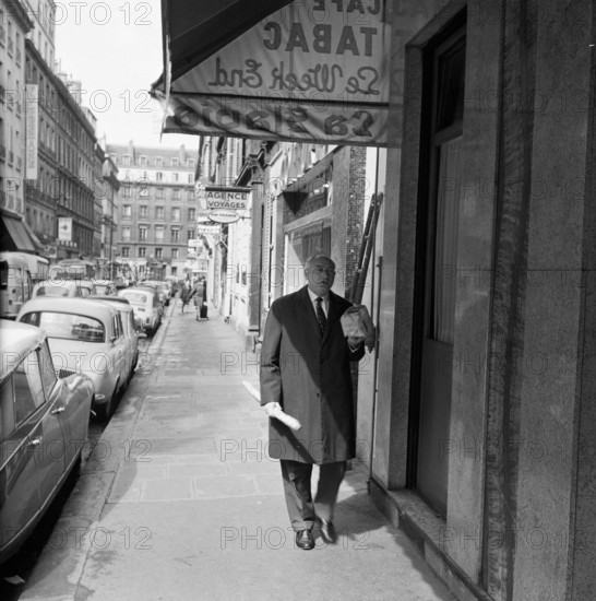 Pariser Bilder [The street life of Paris]  Man with groceries in a shopping street Date: 1965 Location: France, Paris Keywords: groceries, bread, street sculptures, shops