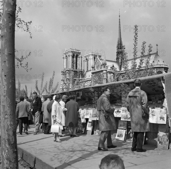Pariser Bilder [The street life of Paris]  Passengers along the bookstalls on the Seine quay, with the Notre-Dame Annotation in the background: The booksellers with a stall along the Seine are called bouquinistes. They sell old books and prints from large chests attached to the parapet Date: 1965 Location: France, Paris Keywords: cathedrals, markets, street images Institution name: Notre Dame