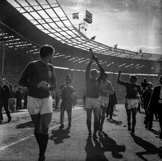 Bobby Moore lifts the Jules Rimet trophy aloft during a lap of honour in Wembley Stadium as the England football team win the FIFA World Cup of 1966, Geoff Hurst, Gordon Banks and Roger Hunt all close by
