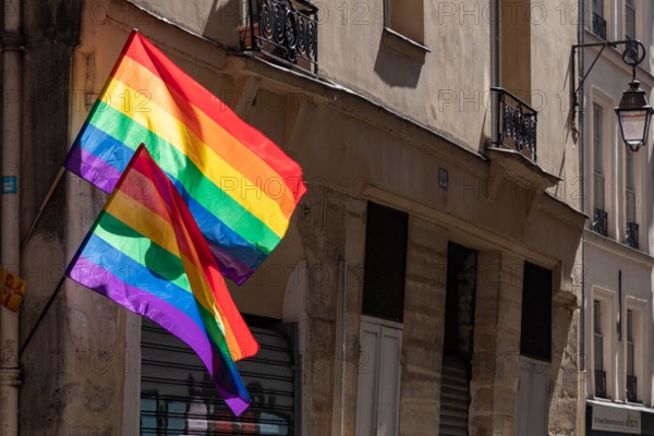 Lgbtq flags hanging at historic building corner during Paris pride. LGBTQIA culture symbol. Bright gay flags waving in wind at sunny day in Paris, Fra