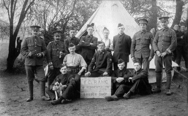 Aldershot, Hampshire. 1914 – British army soldiers of the Regimental Barber Shop, ‘F’ Company, Royal Army Medical Corps at Redan Hill Fort, Aldershot in 1914. The men are posing with their dog mascot in front of a bell tent. Some of the soldiers are wearing standard Khaki with Regimental Police armbands. The rest are wearing temporary blue serge uniforms, known as ‘Kitchener blues’. As a result of the War Office's failure to obtain a sufficient quantity of standard khaki uniforms in the opening weeks of the First World War, this alternative was introduced as an emergency measure.