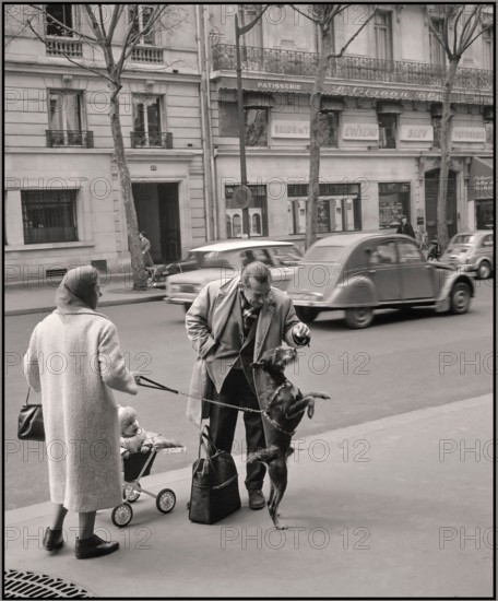 Paris 1965 reportage moment lifestyle fashion street reportage. Citroen Deaux Chevaux passing in background Van de Poll [Street life in Paris] Man playing and feeding the dog of a passer-by 1965  France, Paris