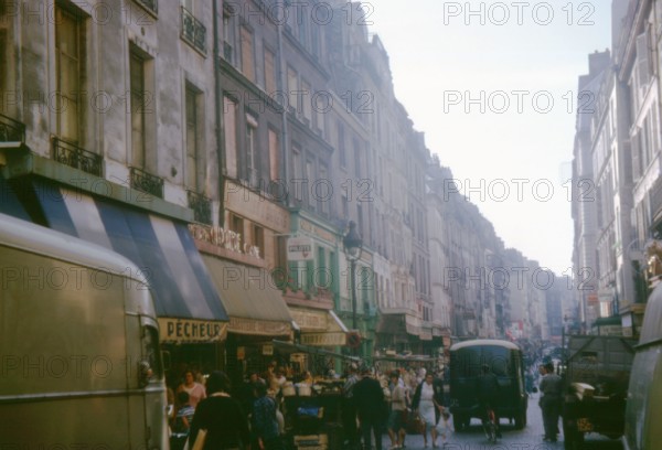 Busy market day on Rue Beaubourg, Paris, France, with shoppers and vintage vehicles. Photographed in September 1964.