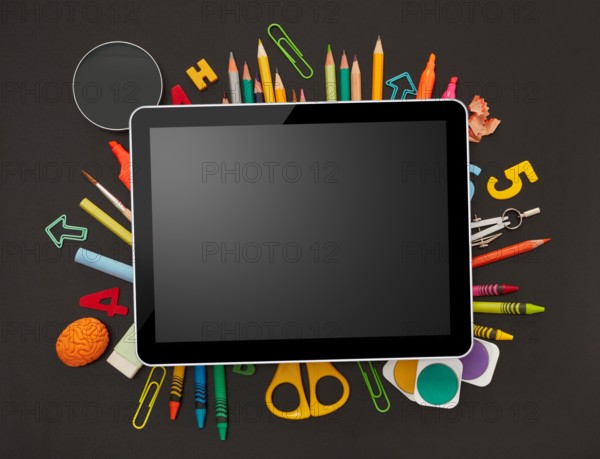 Digital tablet and school supplies on blackboard