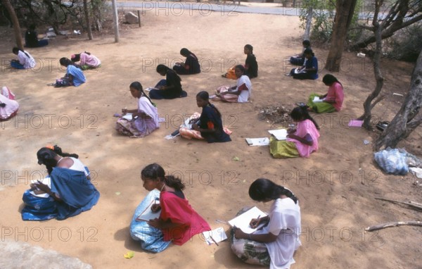 Young students sitting on the ground writing during an outdoor lesson in tamil nadu, India