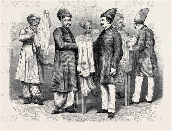 BOMBAY BROKERS AND TRADERS: A "Brokers' room" of an English merchant in Bombay. On the staff of each European firm is a broker, or clerk, acting in the same capacity, whose special business it is to show the goods to the Hindoo buyers, take their bids (which are submitted in a book to the salesman), make bargains, settle disputes, etc. The native way of making and receiving offers is very peculiar, the offer is never made in words, but always by squeezes of the fingers and strokes of the finger across the palm, the hands being covered with a towel or scarf, that bystanders may not know the offer made, as is shown by the two figures in the foreground. 1870