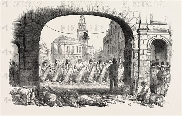 REPAVEMENT OF THE STRAND, LONDON, UK; The usually crowded roadways of Fleet Street and the Strand have just been in part re-laid with granite pavement, in well-timed anticipation of the additional amount of traffic to be expected during the approaching Great Exhibition. The system now generally adopted in the metropolitan carriage roads is, to prepare a foundation of concrete, and then place upon it the granite blocks to a proper curve, generally a flat segment of a circle, so as to throw off the water into the side gutters. The interstices are then grouted with liquid mortar, and the whole surface is afterwards strewed with sand, and thus made ready for traffic., 1851 engraving