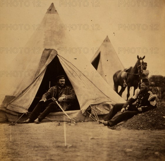 Officer of the 57th Regiment sitting with a sword across his lap at opening to his tent, another officer sitting outside the tent, and a servant stands with a horse in the background, Crimean War, 1853-1856, Roger Fenton historic war campaign photo