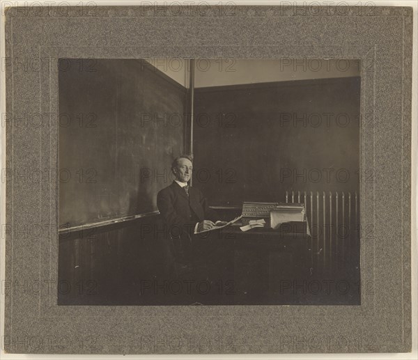 Portrait of a male teacher seated at his classroom desk; American; about 1900; Gelatin silver print