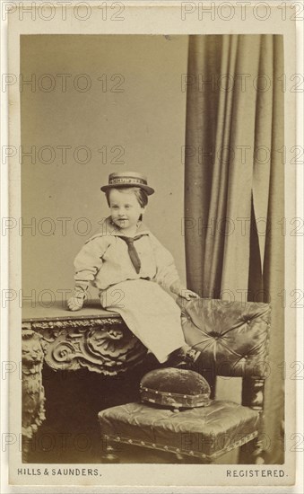 little boy seated on a table, wearing a straw hat with a Speedwell banner; Hills & Saunders, British, active about 1860 - 1920s