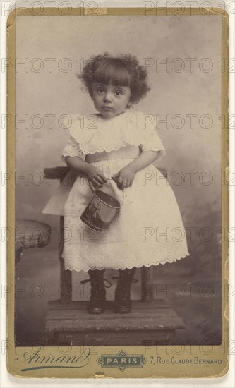 little girl standing in a chair, holding a pail with a ship on it; Armand; 1880 - 1890; Gelatin silver print