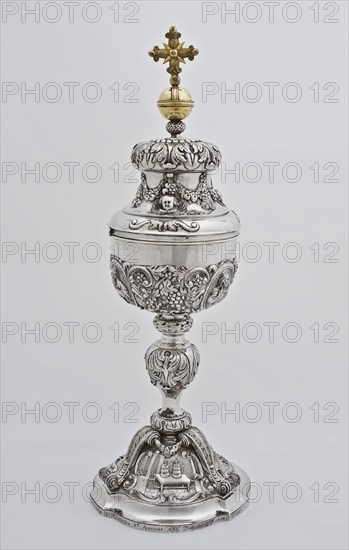 Silver ciborium with lid on which gold-colored cross, ciboric liturgical container holder gold silver, driven chased
