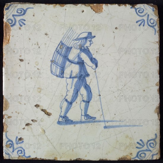 Occupation tile, blue with an image of man with hat and basket with stems on the back and stick in the hand, corner pattern ox