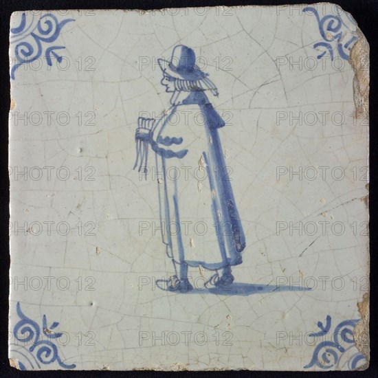 Occupation tile, blue with standing nobleman with handkerchief In his hand, long cloak, top hat, corner pattern ox head, wall