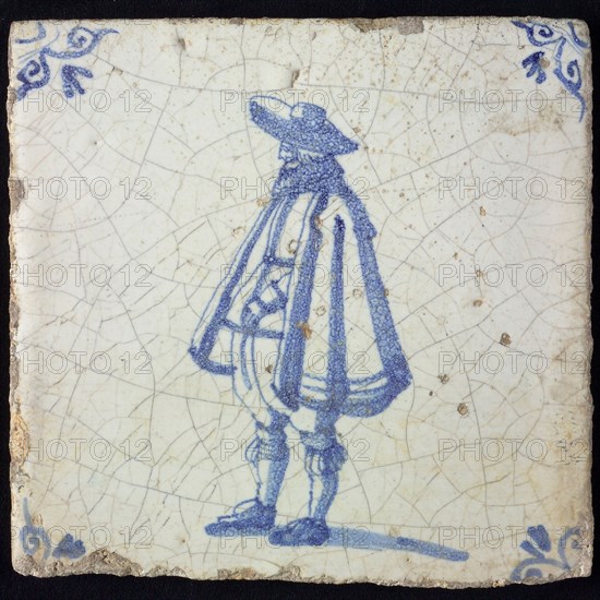 Figure tile, blue with standing man with wide cape and big hat, corner pattern ox's head, wall tile tile sculpture ceramic