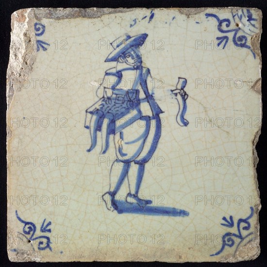 Occupation tile, blue with hawker with chest with merchandise on the hip, corner motif ox's head, wall tile tile sculpture