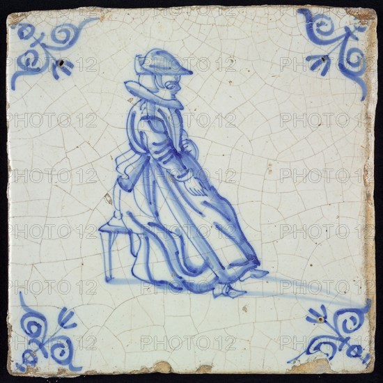 Figure tile, blue with lady sitting on stool, with hat, wide collar and apron, corner pattern ox head, wall tile tile sculpture