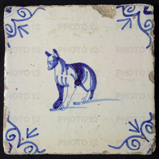 Animal tile, standing dog to the left with strange legs, in blue on white, corner motif ox's head, wall tile tile sculpture