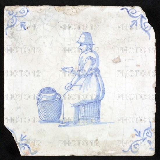 Figure tile, blue with woman sitting on chest with milk jug for her on the ground, corner motif oxen head, wall tile