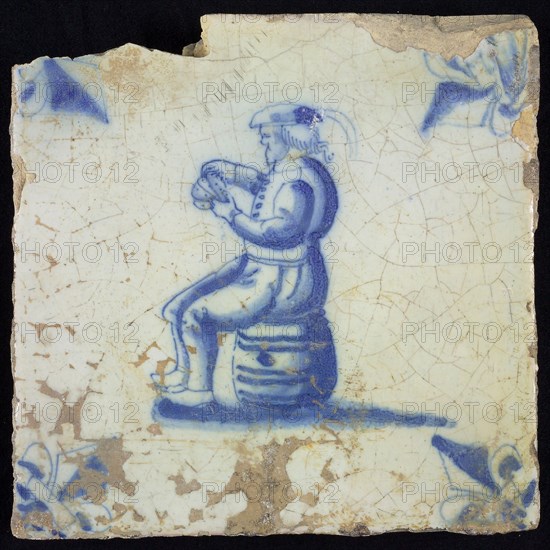 Figure tile, blue with man sitting on barrel with playing cards in hand, corner motif lily, wall tile tile sculpture ceramic