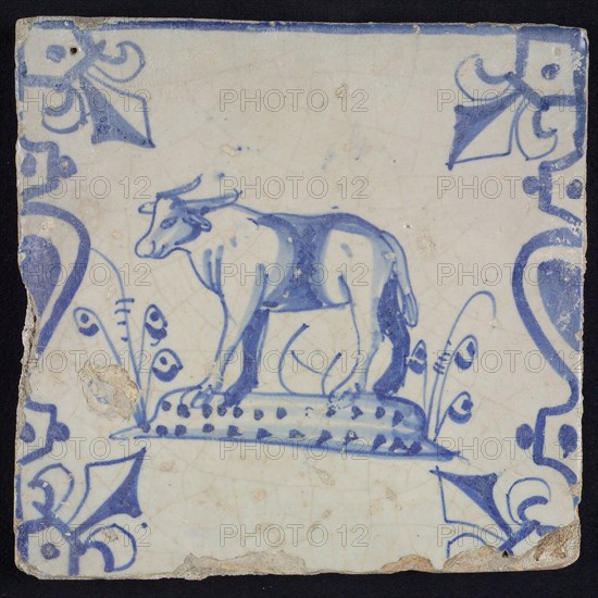 Animal tile, standing ox or cow to the left on plot between balusters, in blue on white, corner pattern French lily, wall tile