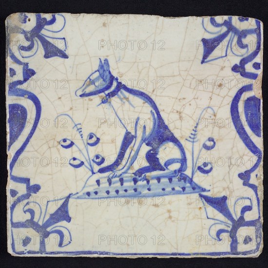 Animal tile, sitting dog to the left on plot between balusters, in blue on white, corner pattern French lily, wall tile