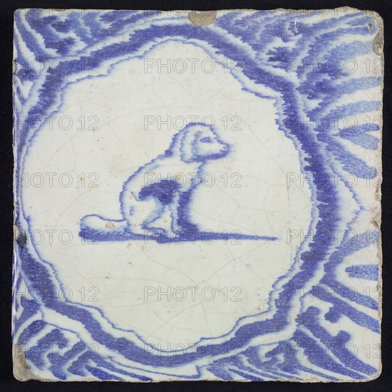 Animal tile, sitting dog to the right inside scalloped frame with braces, in blue on white, corner motif meanders, wall tile
