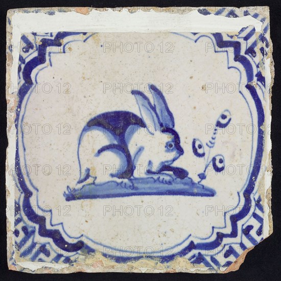 Animal tile, hare to the right on ground within scalloped frame with braces, in blue on white, corner motif meanders, wall tile