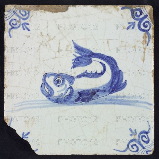 Animal tile, unknown fish in water to the left with open beak and curled tail, in blue on white, corner motif oxen head, wall