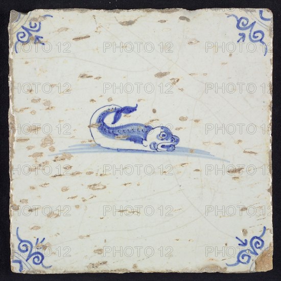 Animal tile, fish in water to the right with open beak and curled tail, in blue on white, corner pattern ox-head, wall tile