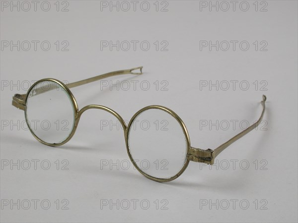 Glasses with round lenses on strength, frame of brass with wide bridge and hinged springs that end in loop shape, spectacle eye