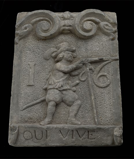 Wall brick from gate with musketeer and ribbon with text qui vive 16, facing stone sculpture sculpture building component