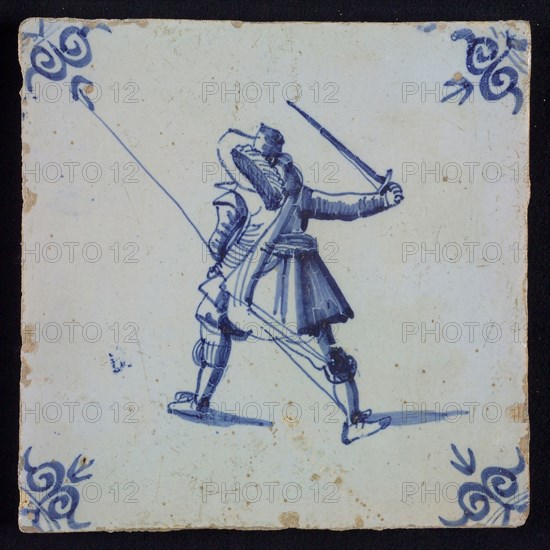 White tile with blue warrior with plume hat, spear and raised sword, seen from behind; corner pattern ox head, wall tile