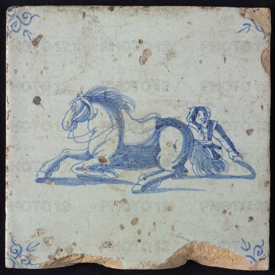 White tile with blue horseman, lying horse, man kneeling behind it; corner pattern ox head, wall tile tile sculpture ceramic