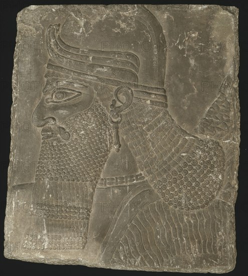 Relief Showing the Head of a Winged Genius, Neo–Assyrian Period, reign of King Ashurnasirpal II (883 BC–859 BC), Mesopotamian, Assyrian, Nimrud, Gypsum relief with traces of pigment, 68 × 59 × 4.5 cm (26 1/2 × 23 × 2 in.)