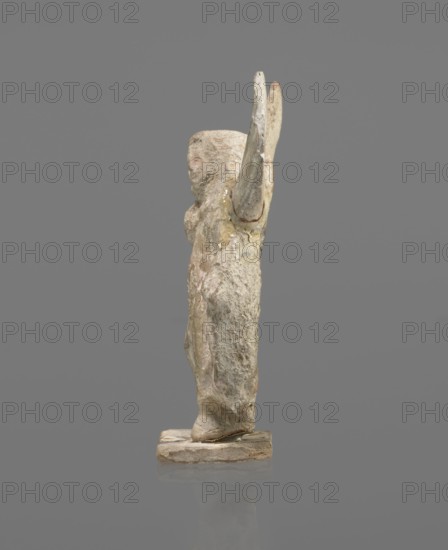 Terracotta figurine of Psyche, Young Psyche with butterfly wings, wrapped in a chlamys. Right hand rests on the chest, left hand rests along the body. Long hair falling on the shoulders is arranged in curls. Head turned to the left. Figurine placed on a rectangular base. 332–30 BC; Hellenistic period. Tanagra Greece. Figurine; height 10.8 cm, width 7.5 cm, depth 3 cm., A small worn statue of a standing figure seen in profile on a rectangular base, with an arm raised behind the head and a rounded head with indistinct facial features; the surface shows rough, weathered texture with patches of pale beige, off-white, muted pink, and light gray, along with some darker beige and brown areas, all set against a solid gray background.